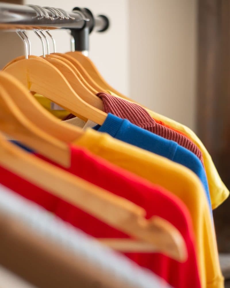 A row of t-shirts on wooden hangers in different colours