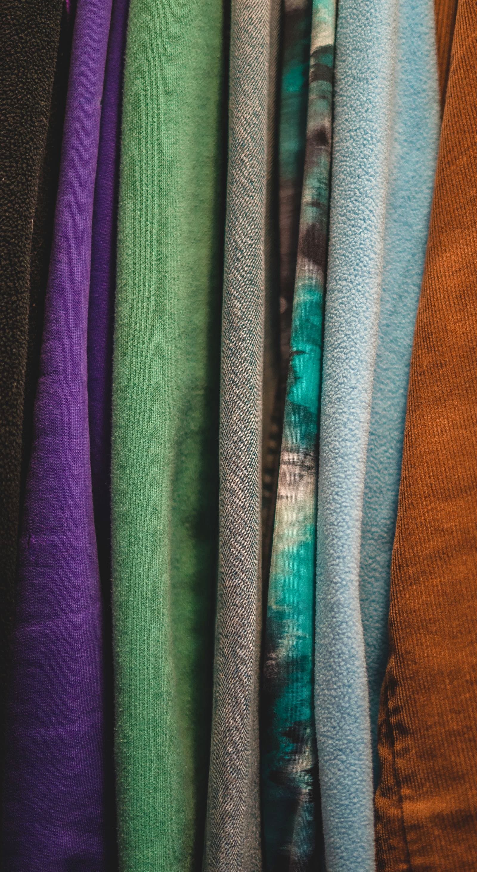 A vertical stack of colorful folded fabric in shades of purple, green, teal, blue and rust